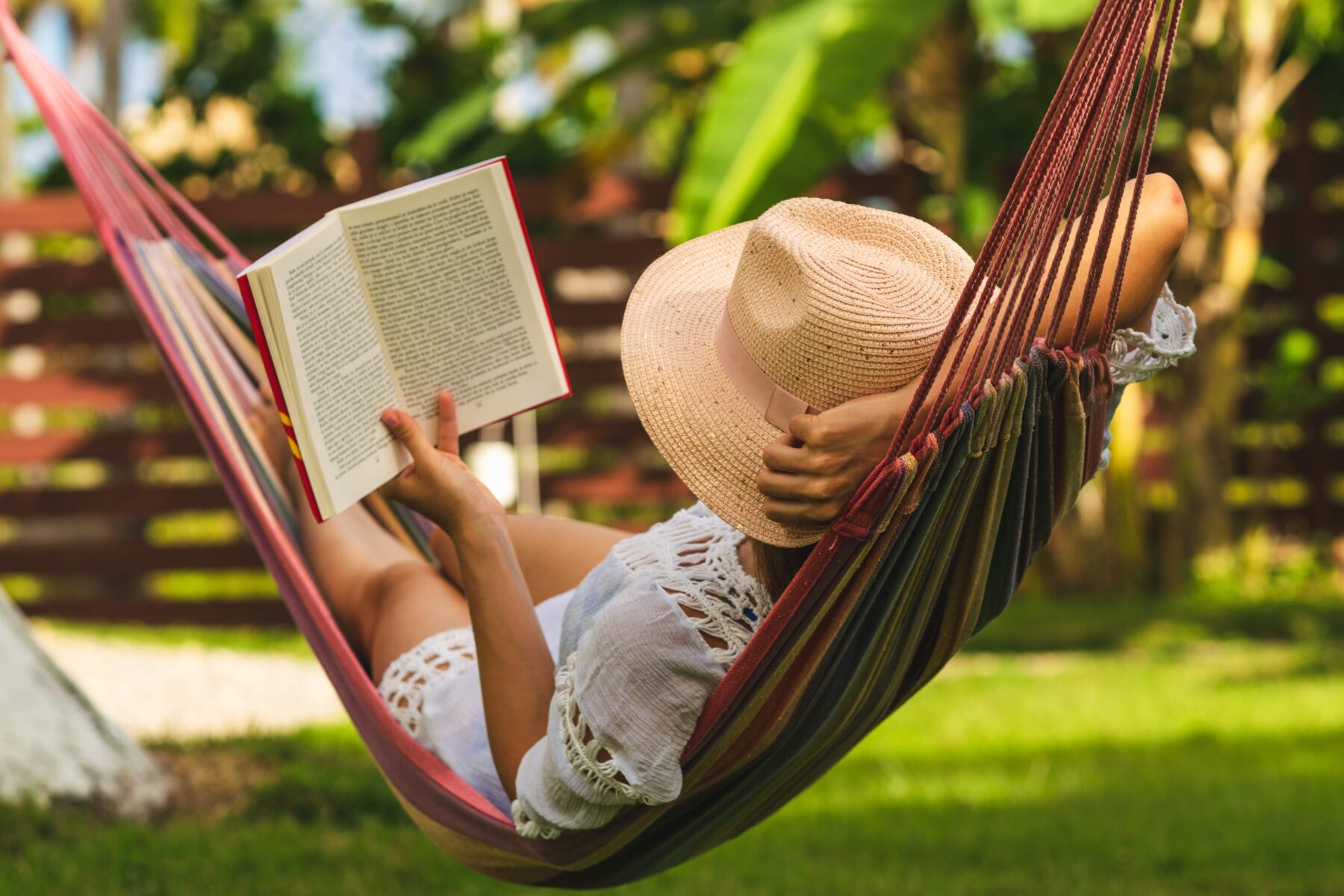 woman laying down in a hammock reading a book on a sunny day