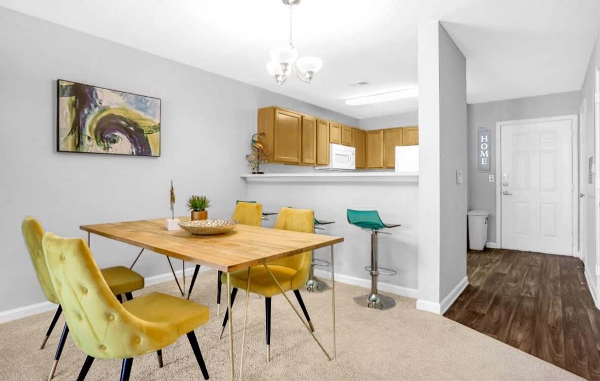 Dining room apartment space with table and four chairs, next to bar height table with three stools attached to kitchen.