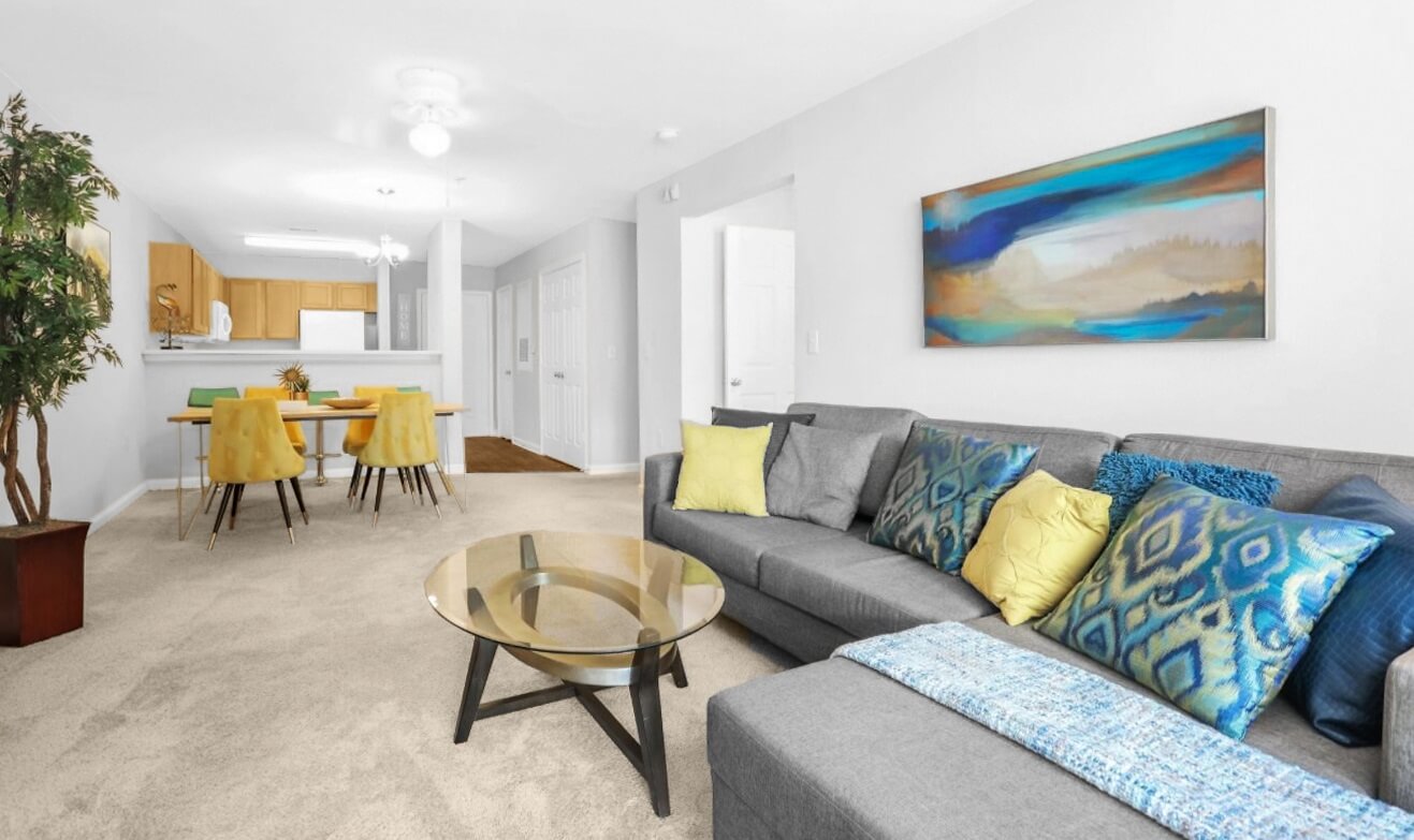 Living room with sectional sofa, dining room with four chairs and a view of the kitchen and front door.