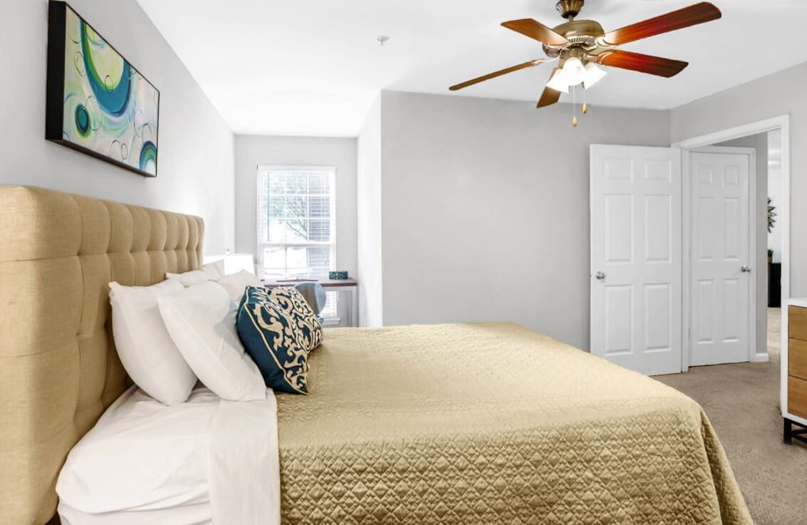Bedroom with fan chandelier, bed, and corner with writing desk underneath window.