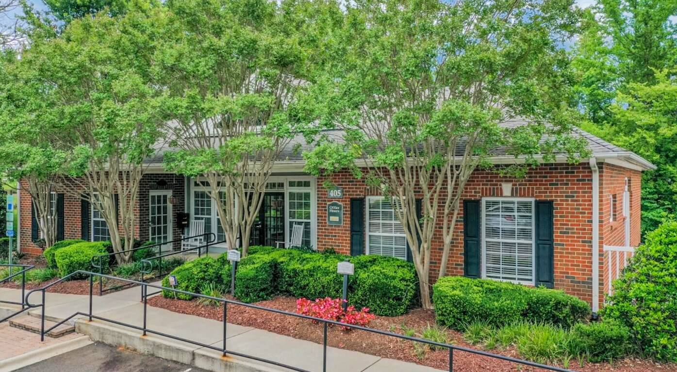 Brick leasing office exterior with accessible ramp and lush foliage and landscaping.