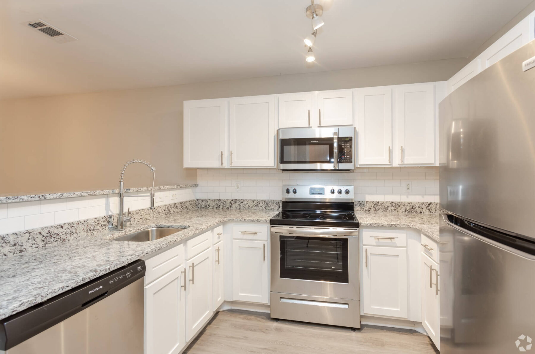 Wrap around kitchen with stainless steel appliances, overhead microwave, granite countertops and white cabinets.